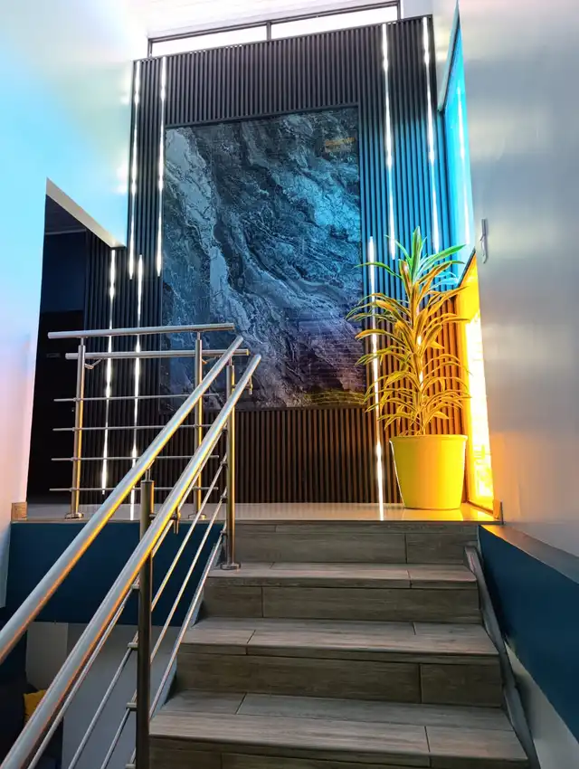 Escalera interior con barandal de acero inoxidable, listones oscuros y luz cálida